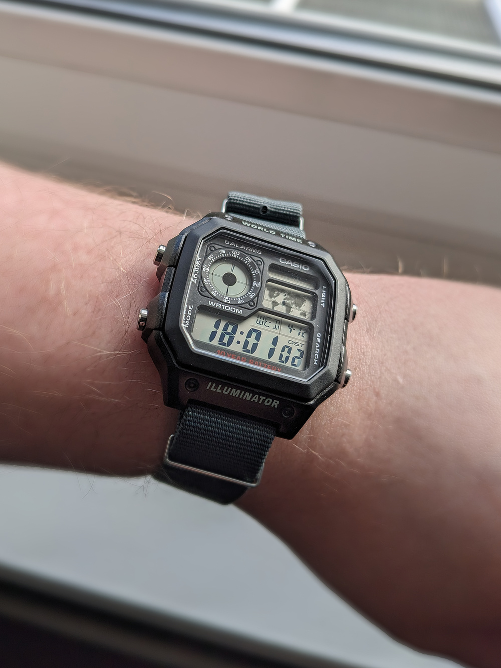 A photograph of a digital watch - a Casio AE-1200 - on my wrist. The time reads 18:01, with the date marked as the 12th of April.