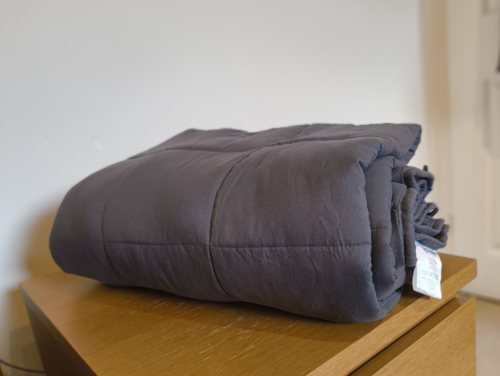 A weighted blanket folded up on top of a nightstand. There are notable pillow-shaped extrusions across its surface. 